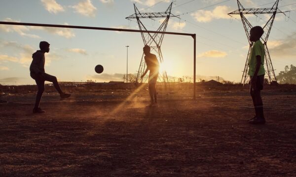 young african boys playing soccer football in an informal settlement township on dirt field